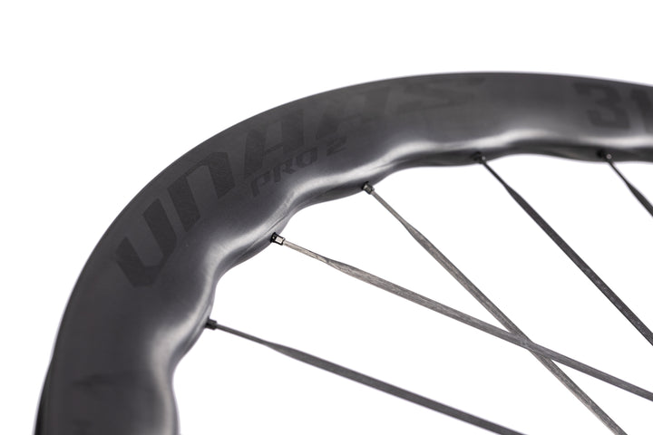 UNAAS Pro2 carbon bike wheel with distinctive wave rim and matte black finish on white background.