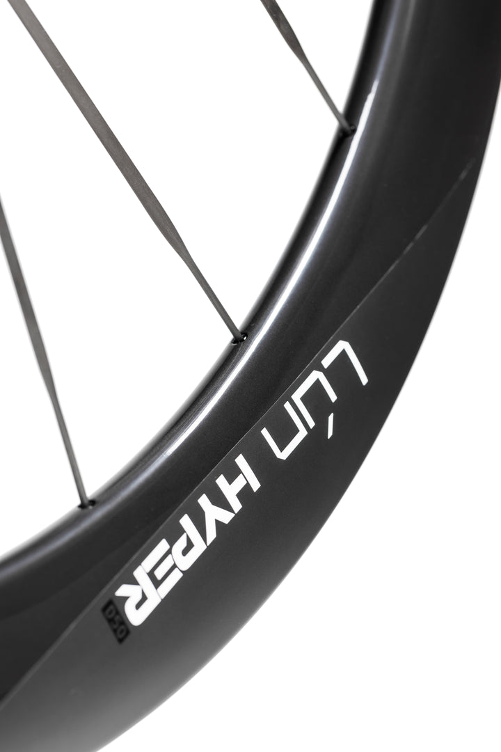Matte black LUN HYPER 5 carbon fiber bicycle wheel with thin dark spokes and white branding on rim. Showcasing design.