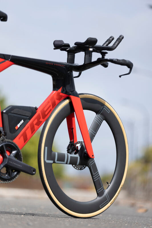 Lún Kronos tri-spoke carbon wheel on red time trial bike with tan tire and LUN logo.
