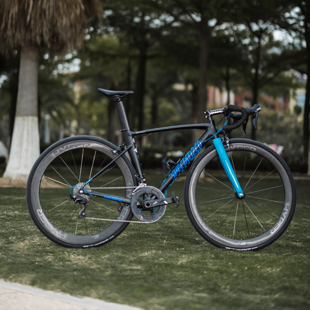 Road bicycle with Lún HYPER 23 SE R67 carbon rim brake wheelset, black frame with blue accents, parked on grass.