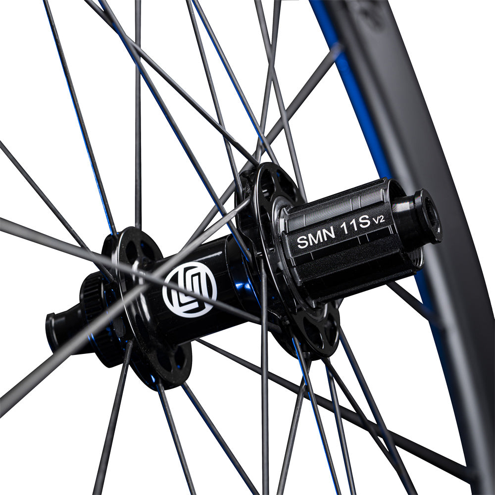 Close-up of Lún Routte SE road bike wheel hub showing black finish, white L logo, SMN 11S V2 freehub, and spokes.